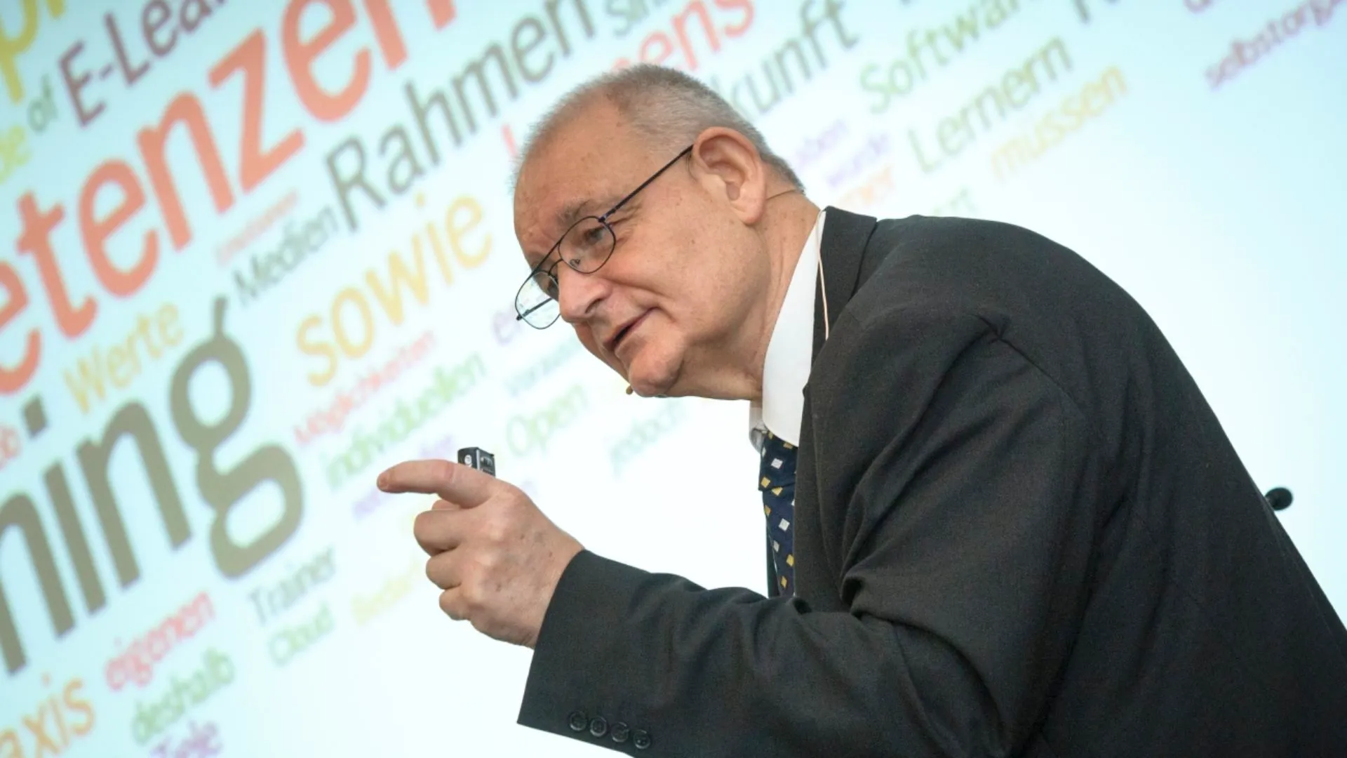 Prof. Dr. John Erpenbeck bei einem Vortrag vor einer Wortwolke zu Kompetenzen
